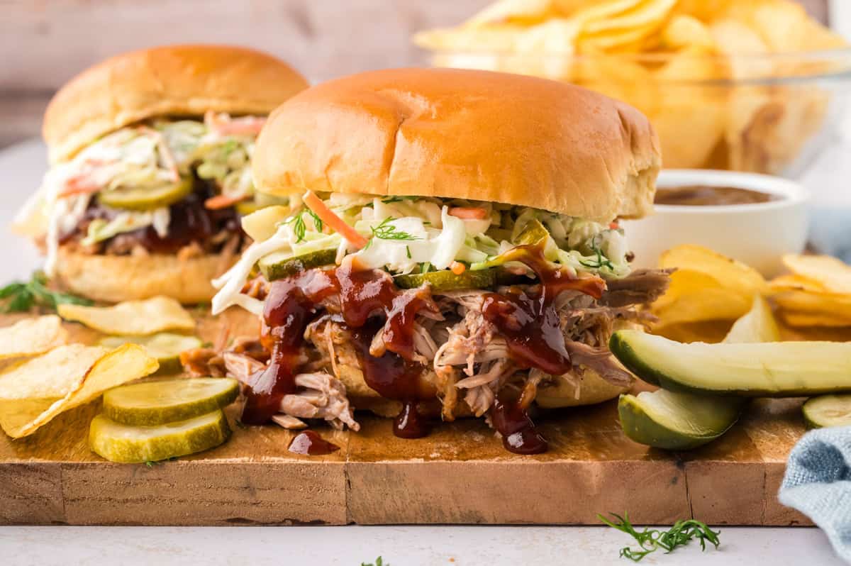 A close up of a pulled pork and coleslaw sandwich on a wooden cutting board.