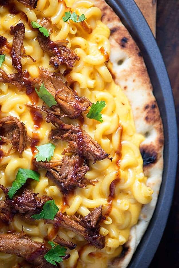 A close up of a mac and cheese pizza with pulled pork pizza on a pizza pan.