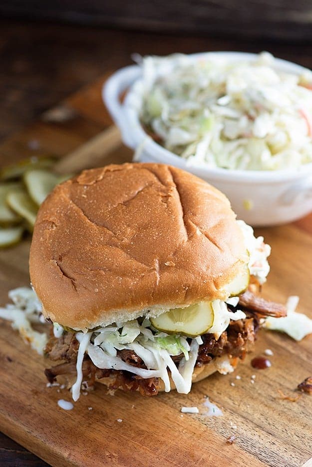 A pulled pork sandwich on a cutting board with a small white cup of coleslaw.