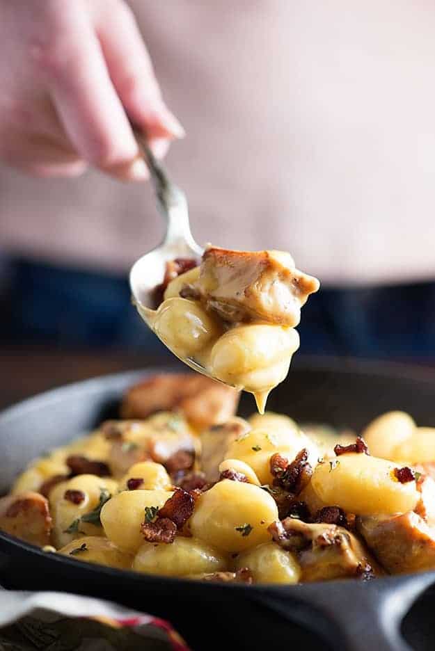 A spoonful of pork gnocchi held above a skillet of cheesy gnocchi.