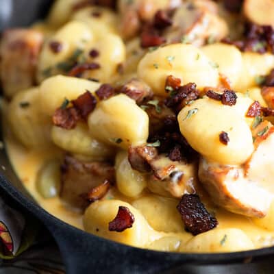 A cast-iron skillet with cheesy gnocchi and bacon in it.