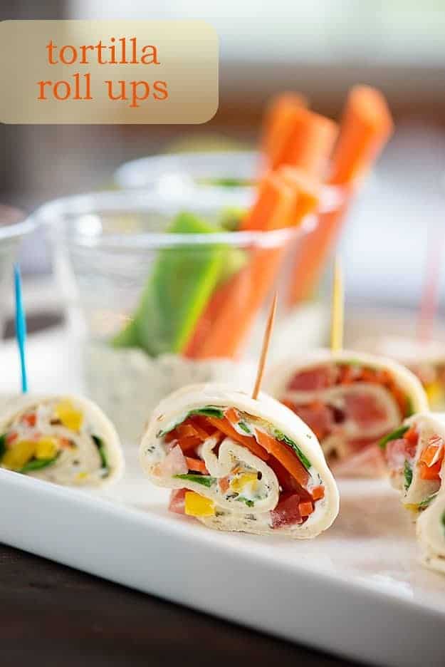 Several tortilla roll-ups filled with vegetables.on a flat white serving tray.