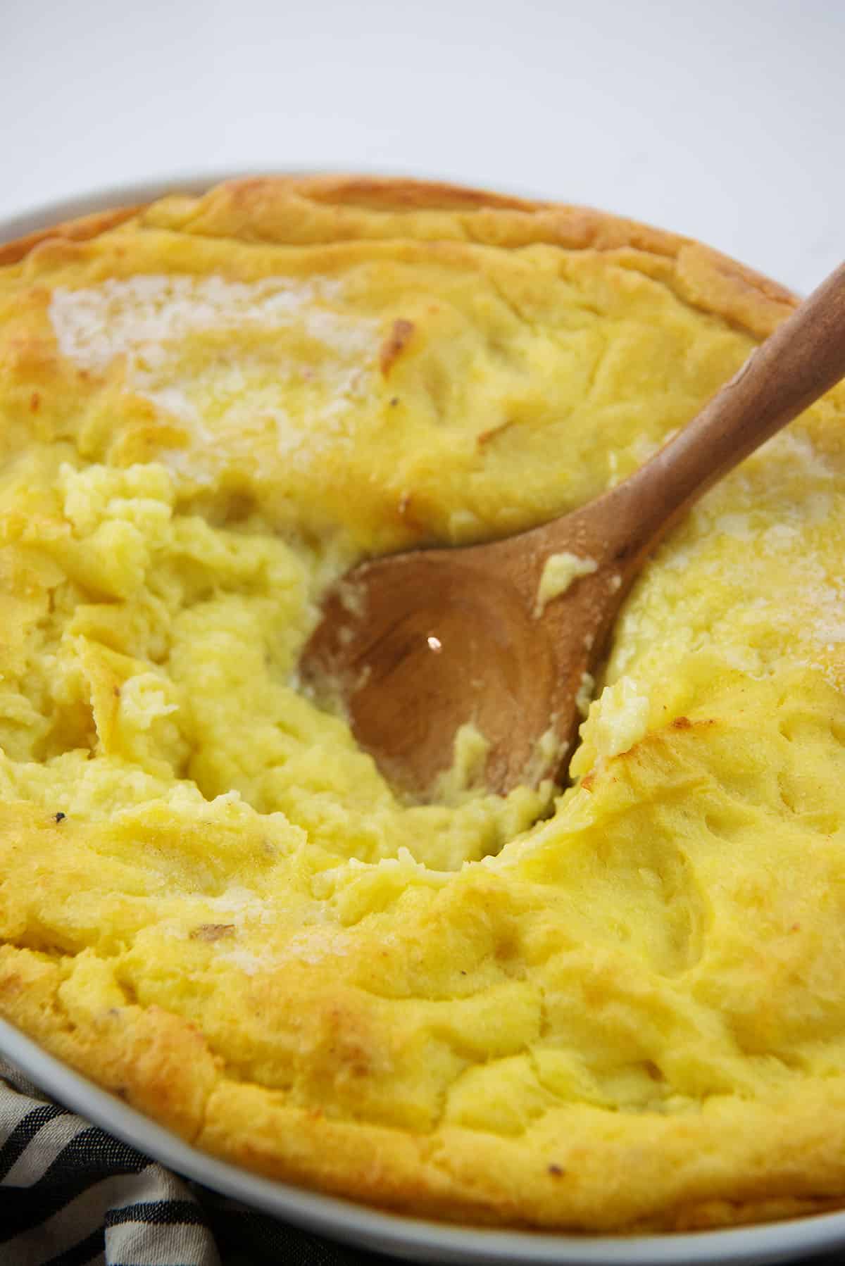 wooden spoon in dish full of mashed potatoes.