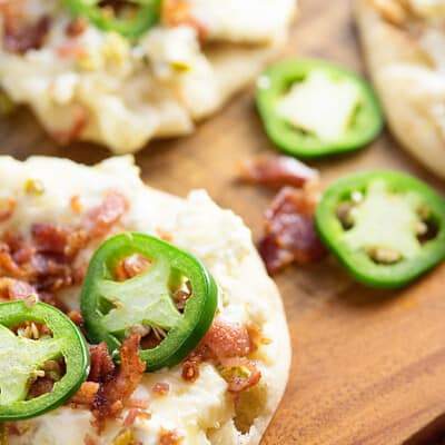 Jalapenos spread throughout a cutting board full of jalapeno popper flatbread.