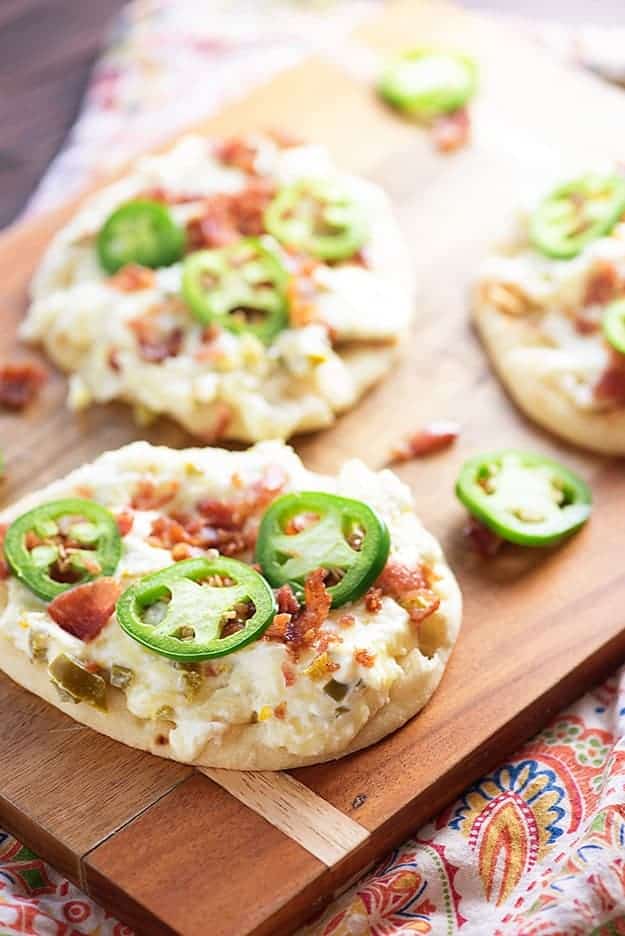 Three jalapeno popper flatbreads on a wooden cutting board.