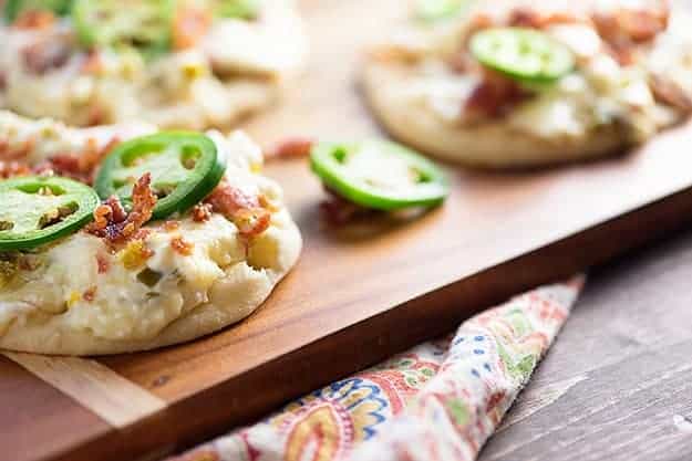 A flatbread topped with jalapenos on a wooden cutting board.