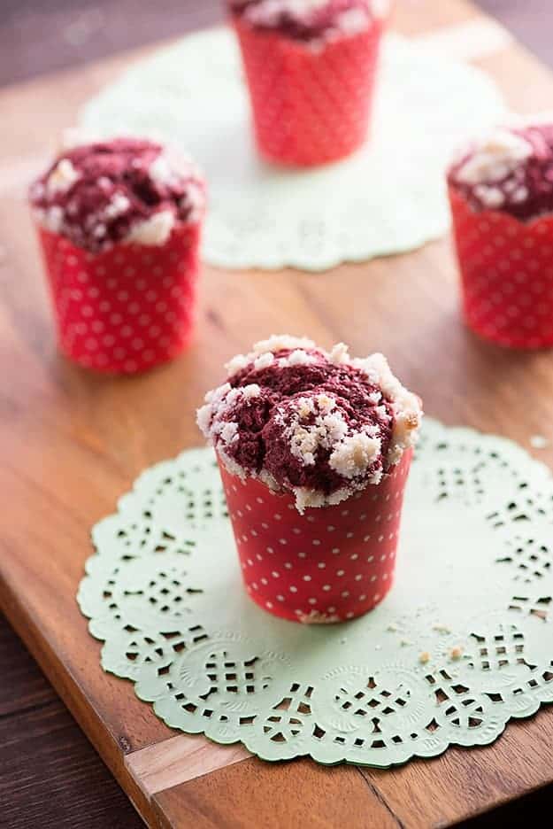 A wrapped red velvet muffin on a white lace place holder on a wooden table.