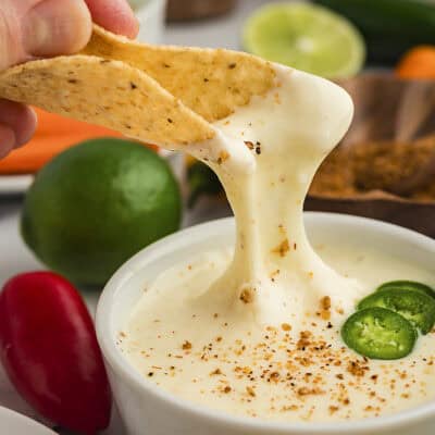 White queso dip dripping off tortilla chiip.