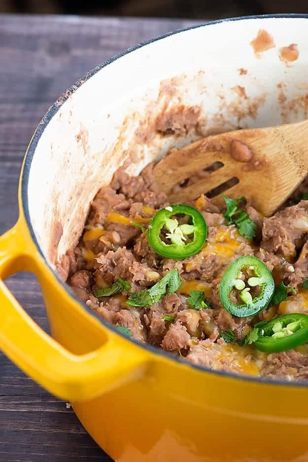 A wooden spoon stirring refried beans in a large pot.