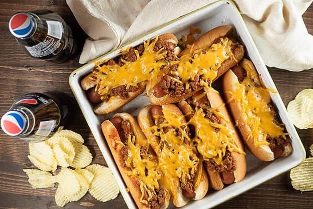 A baking pan full of hotdogs covered in shredded cheese.