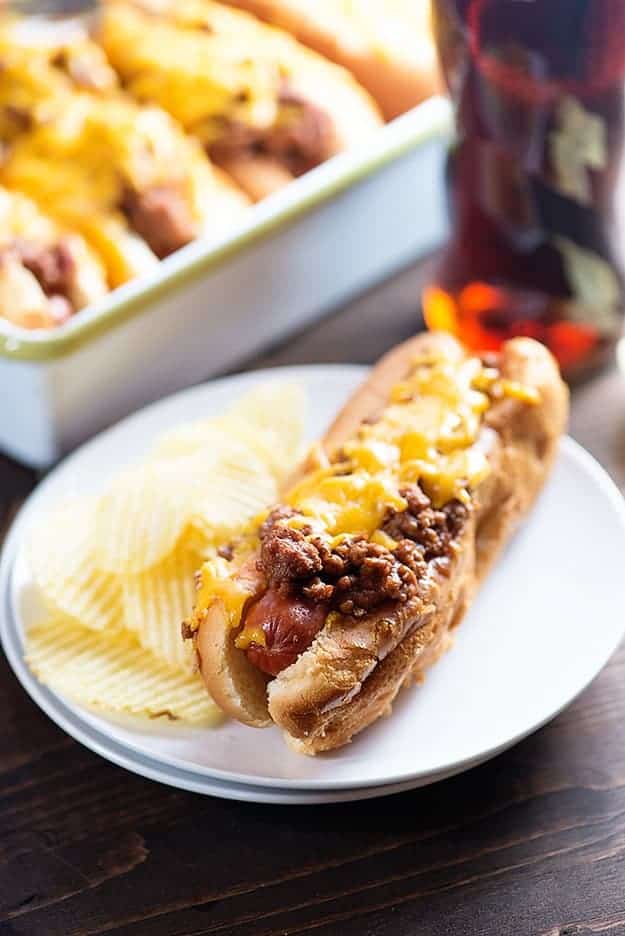 A sloppy joe hot dog on a plate with some rippled potato chips.