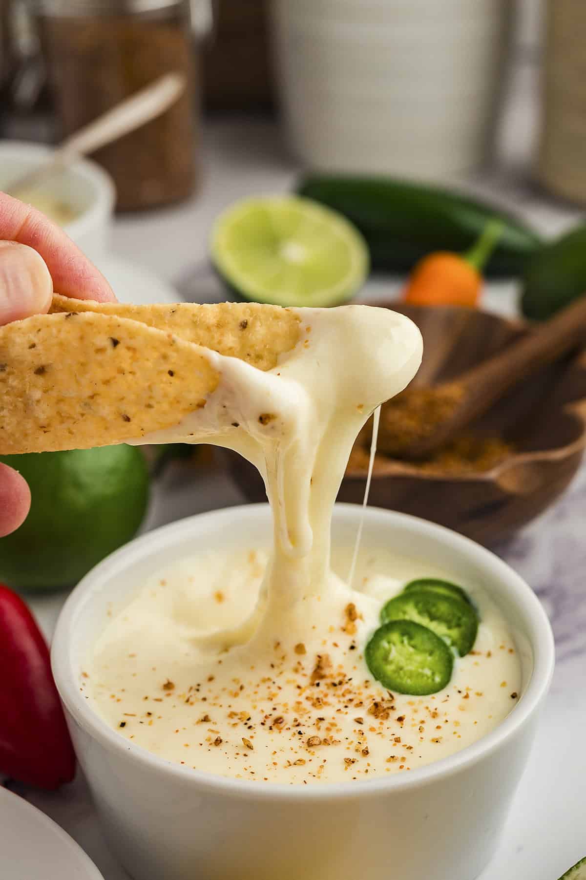 A close up of a taquito being dipped into a white queso dip.