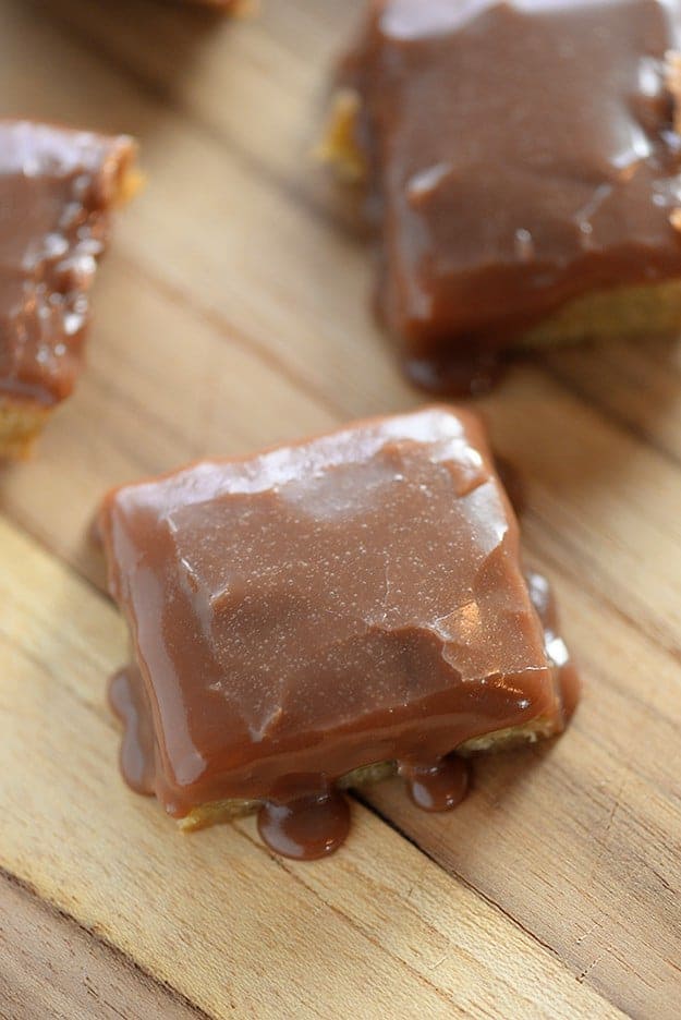 chocolate frosted blondies on top of a wooden cutting board.