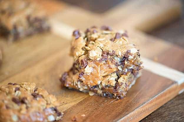 A close up of a couple of peanut butter caramel bars on a cutting board.