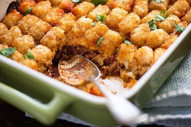 A dish of tator tot casserole with a serving removed.