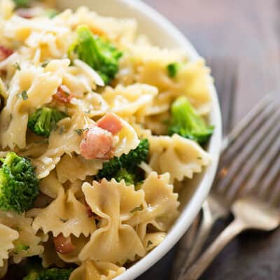 Brocolli and bowtie pasta in a white bowl next to two silver forks.