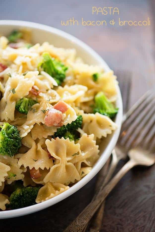 Brocolli and bowtie pasta in a white bowl next to two silver forks.