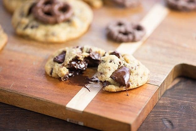 A chocolate chip cookie cut in half on top of a wooden cutting board.