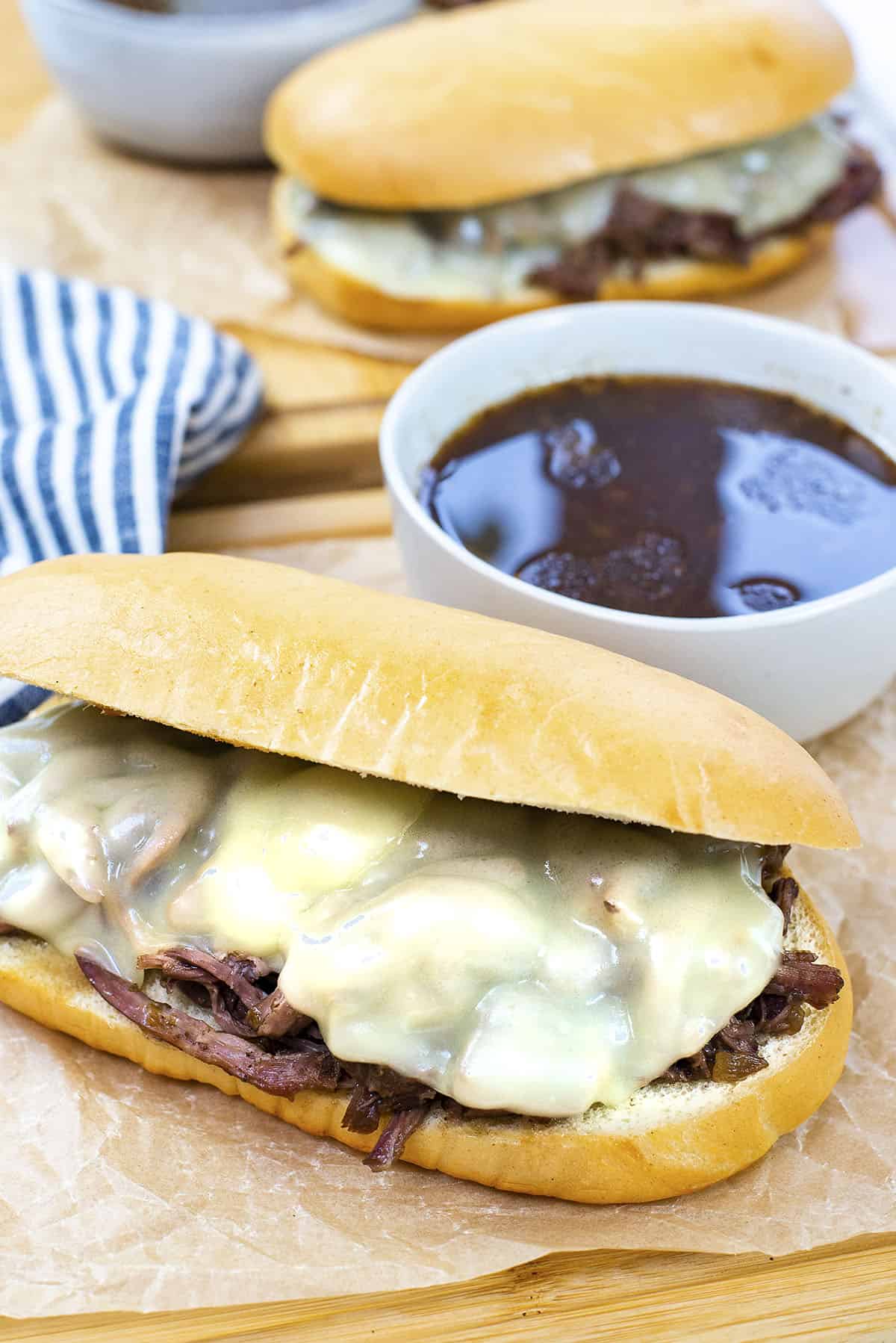French dip sandwich on wooden board next to dipping sauce.