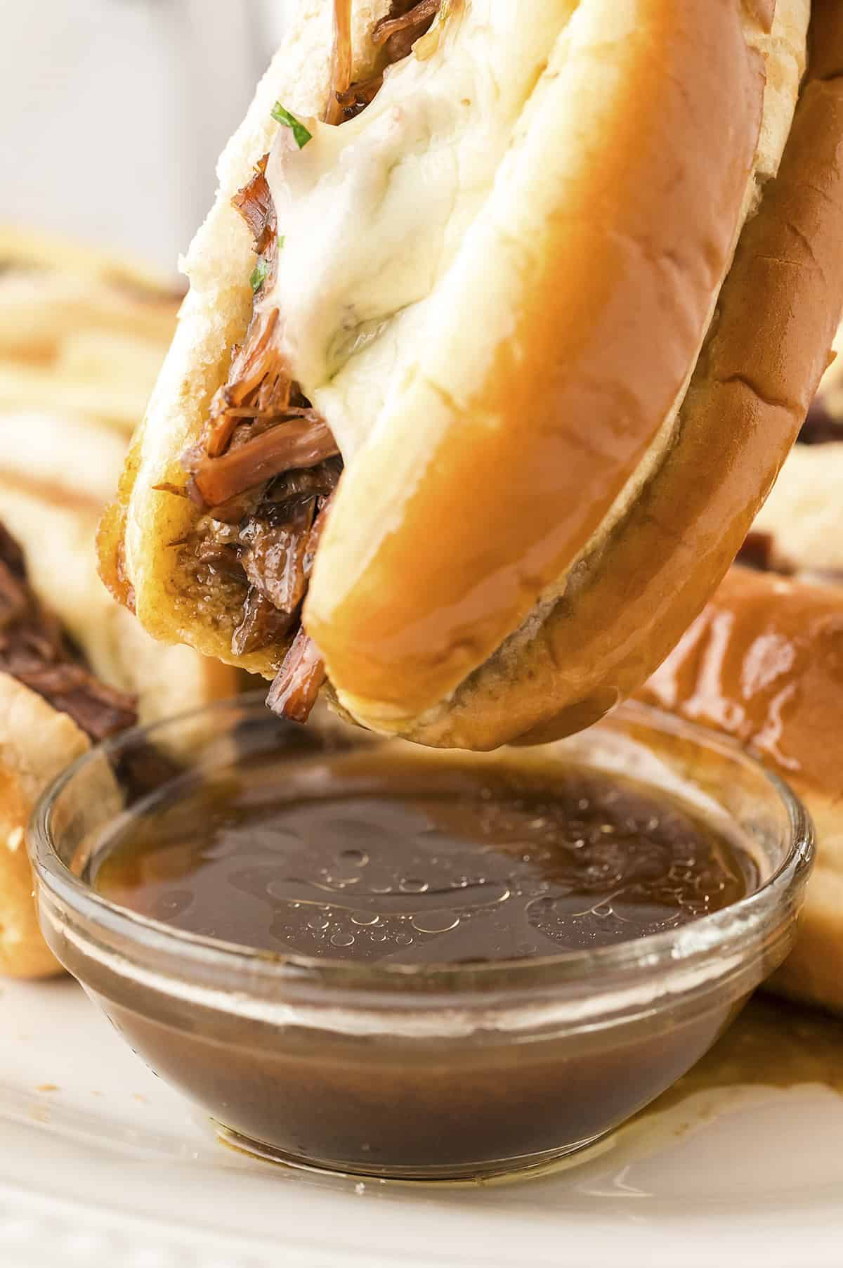 French dip sandwich on wooden board next to dipping sauce.