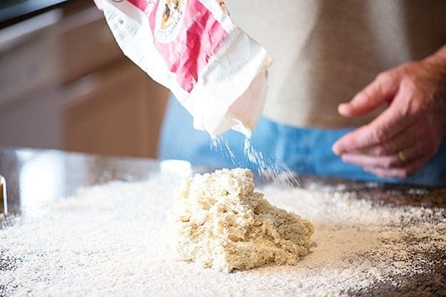 man sprinkling flour onto biscuit dough.