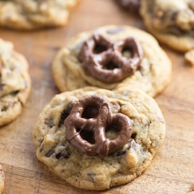 A close up of cookies topped with chocolate covered pretzels on a wooden cutting board