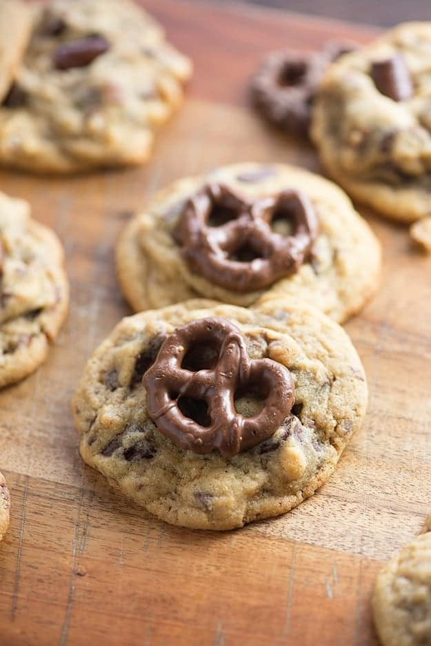A close up of cookies topped with chocolate covered pretzels on a wooden cutting board