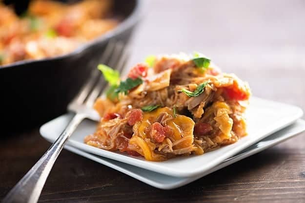 A square white plate with pulled pork on it.