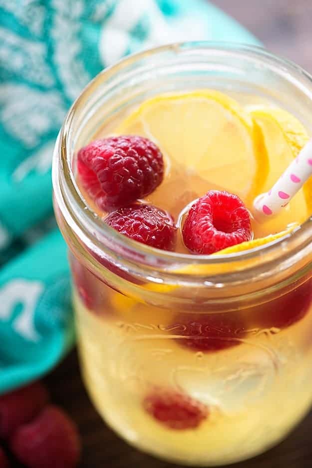 A clear glass jar with fruits and a polka dot straw in it.