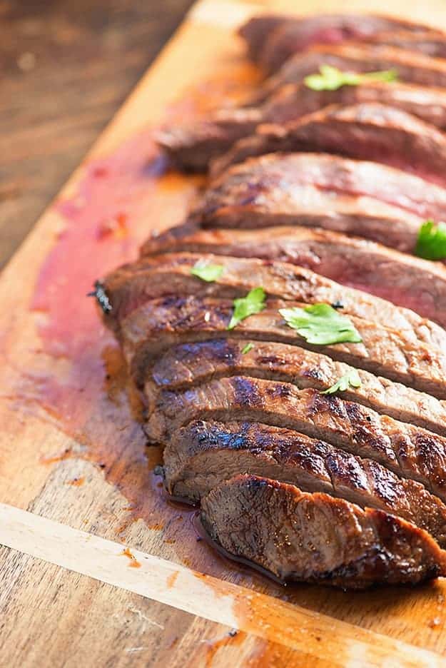 A cut flank steak on a wooden cutting board.