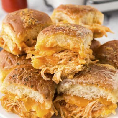 Buffalo chicken sliders stacked on a white plate.