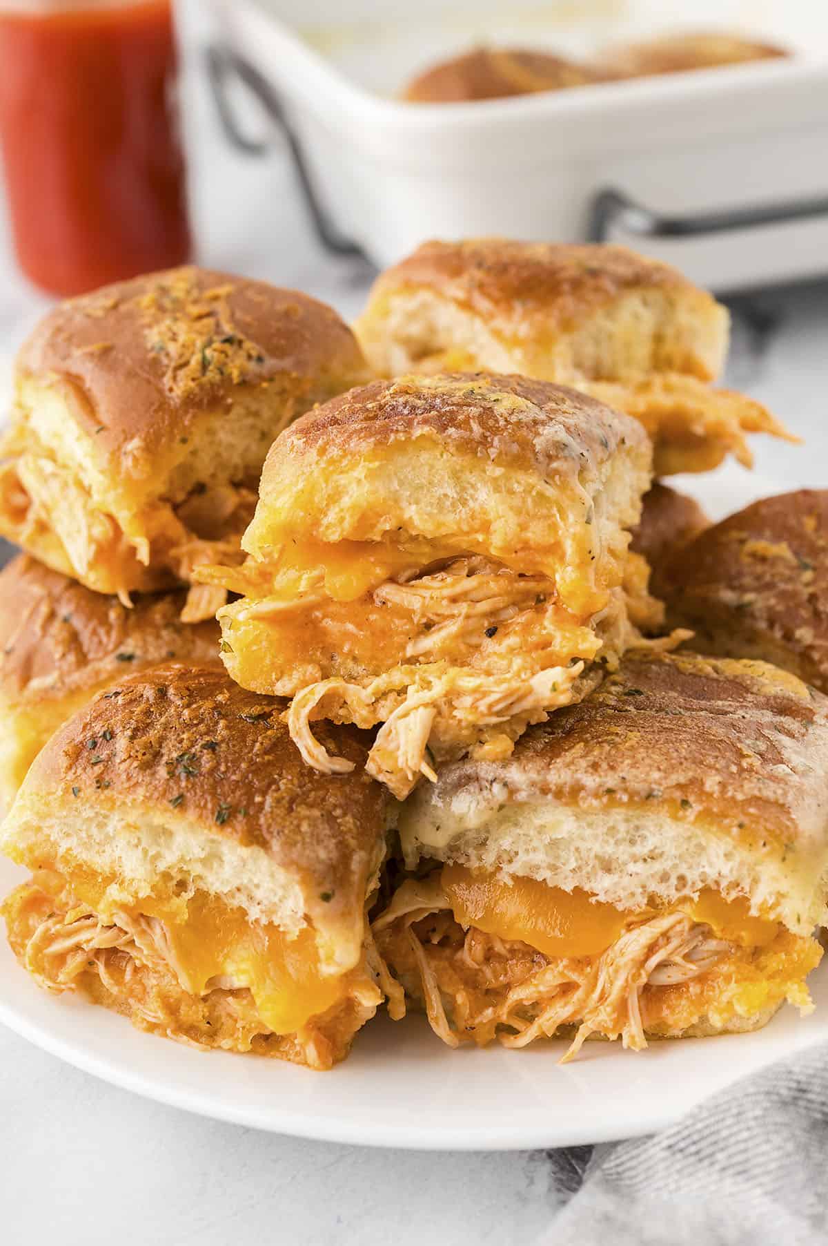 Buffalo chicken sliders stacked on a white plate.