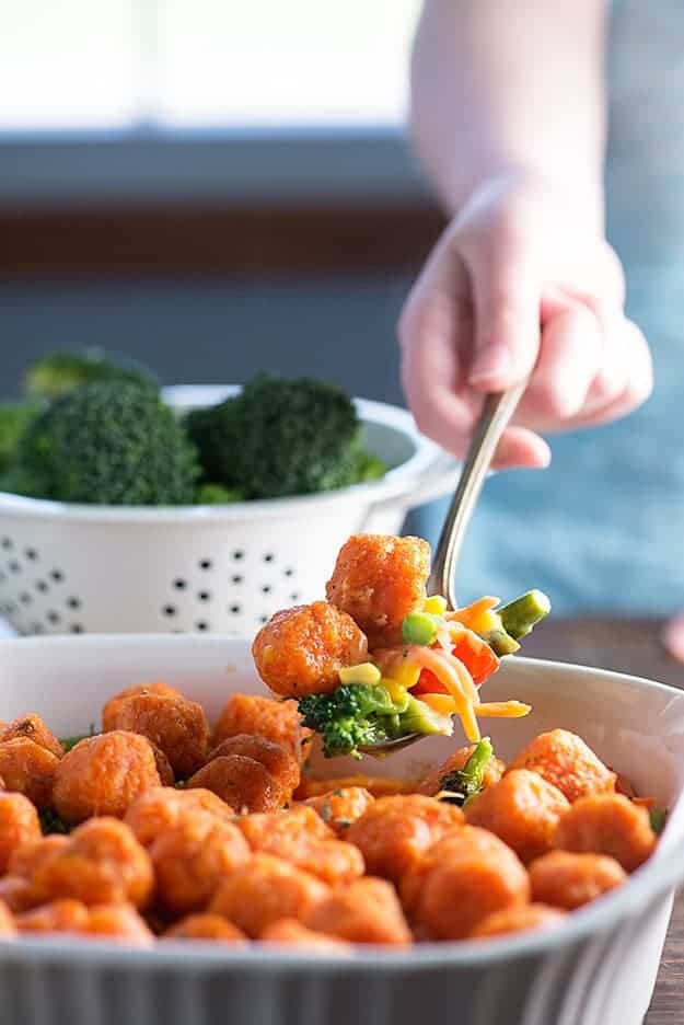 A person using a large spoon to scoop up some tater tots and vegetables.