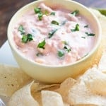 Cream cheese salsa in a cup next to a plate of tortilla chips.