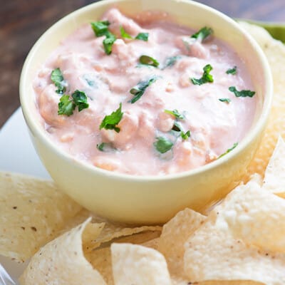 Cream cheese salsa in a cup next to a plate of tortilla chips.