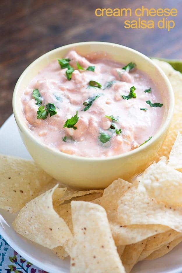 Cream cheese salsa in a cup next to a plate of tortilla chips.