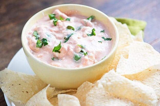 Cream cheese salsa in a cup next to a plate of tortilla chips.