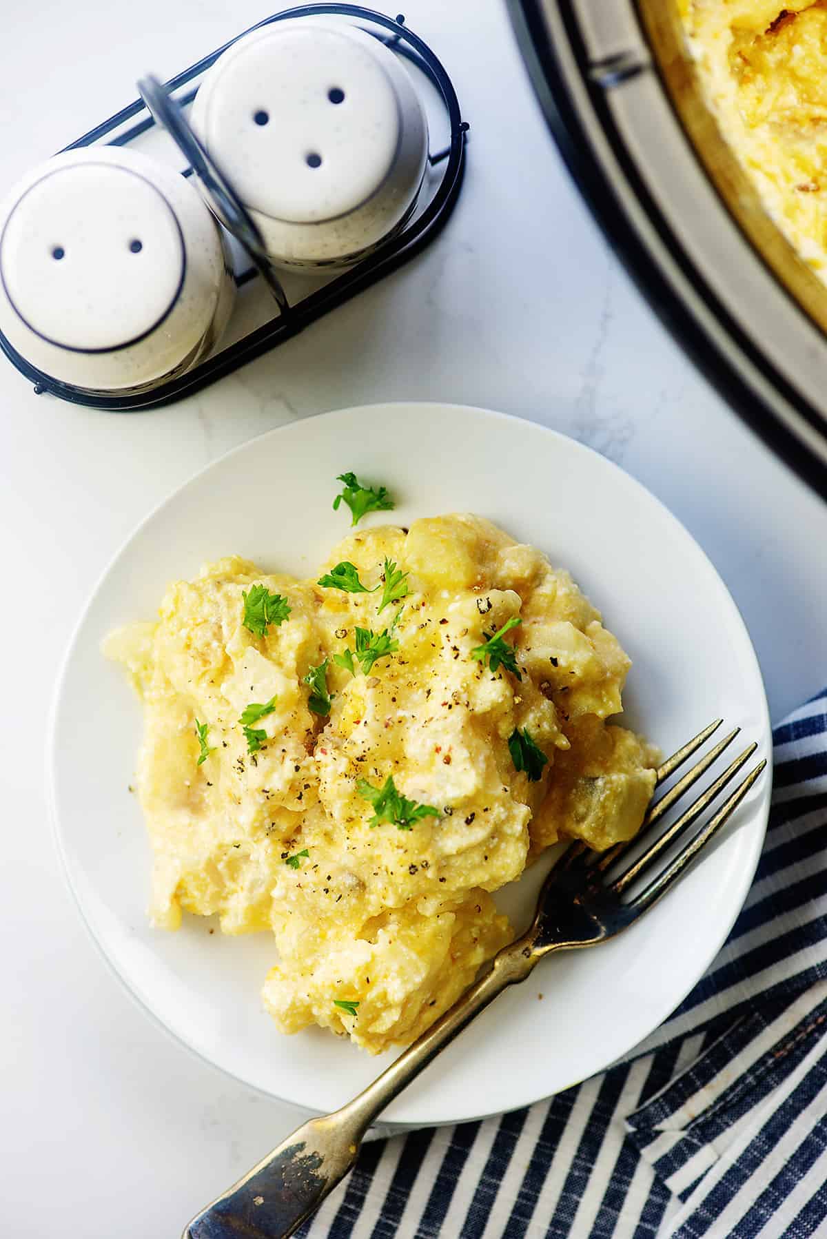 hashbrown casserole on white plate next to a crockpot.