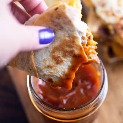 A woman holding a quesadilla above a jar of ketchup.