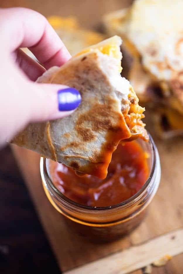 A woman holding a quesadilla above a jar of ketchup.