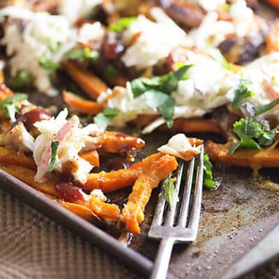 A fork on a baking sheet of loaded sweet potatoe fries.