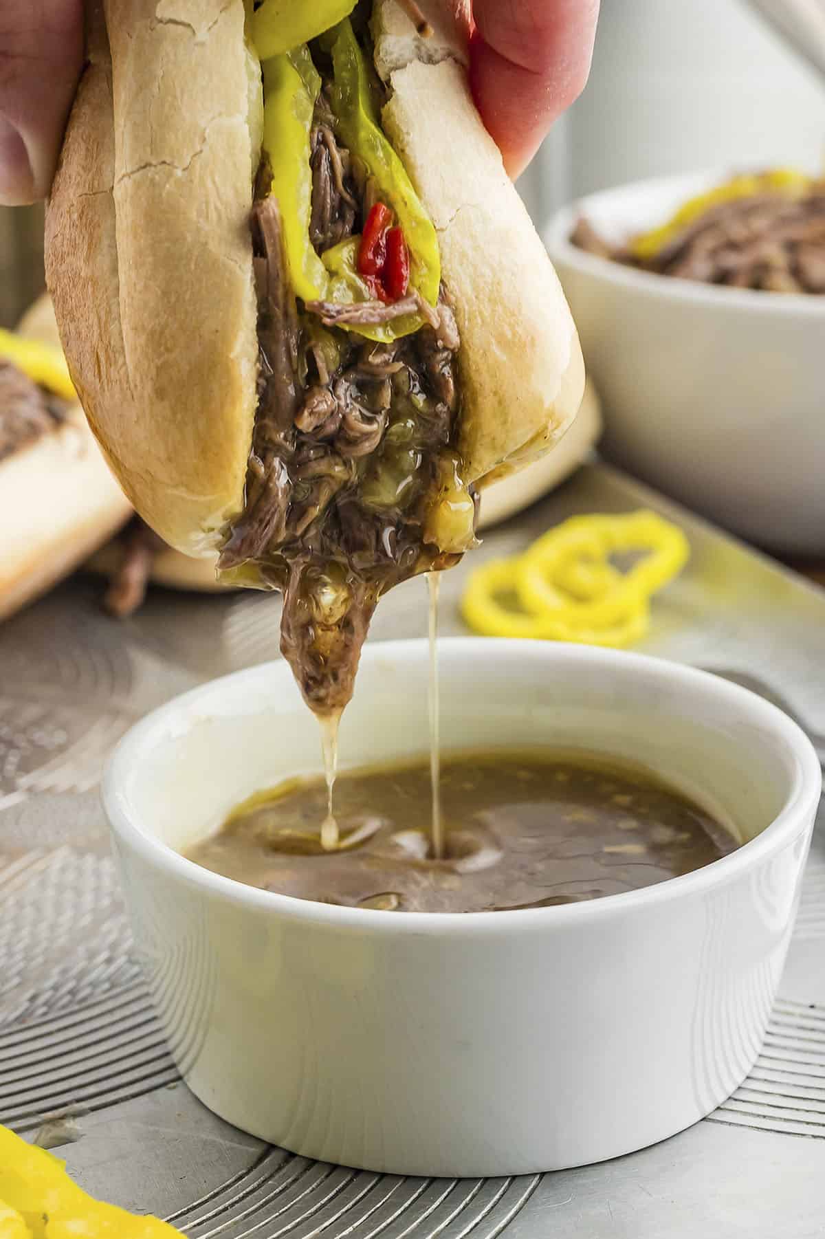 Italian beef sandwich being dipped in juice from meat.