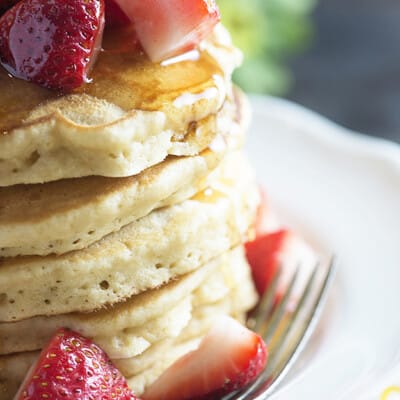 A close up of strawberries spilling over the side of a stack of pancakes.