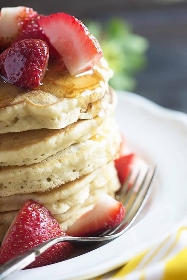 A close up of strawberries spilling over the side of a stack of pancakes.