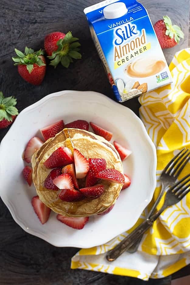 Overhead view of strawberries on top of pancakes on a white plate.