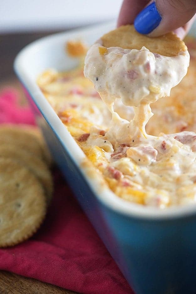 A ritz cracker dipped into a pan of baked pimento cheese.