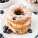 Stack of blueberry donuts on small white plate.