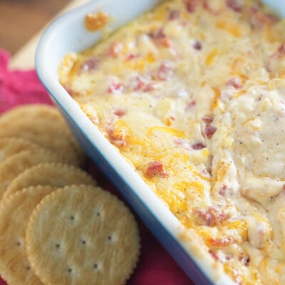 A baking dish of cheese dip next to a ritz cracker.