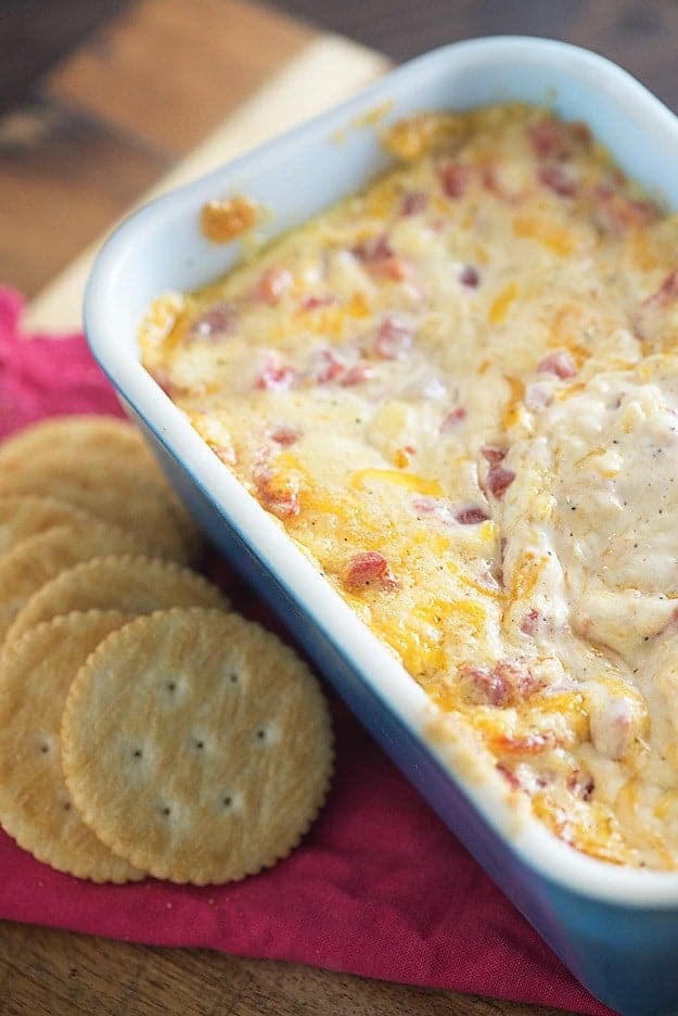 A baking dish of cheese dip next to a ritz cracker.