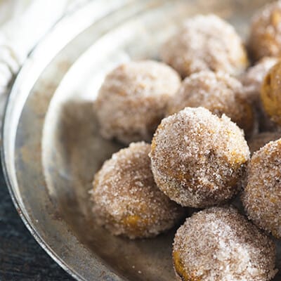 A pile of donut holes on a clear glass pie plate.